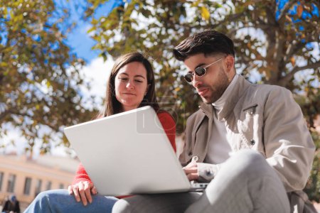 Deux étudiants utilisant un ordinateur portable dans le parc du campus, vue rapprochée d'en bas. Génération Z. Photo de haute qualité