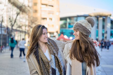 Téléchargez les photos : Forger des amitiés urbaines : deux jeunes femmes marchant dans la ville, fermant les yeux et partageant des sourires - en image libre de droit