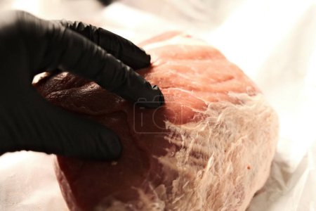 Téléchargez les photos : Main en gant noir touchant filet de porc cru sur la planche de cuisine - en image libre de droit