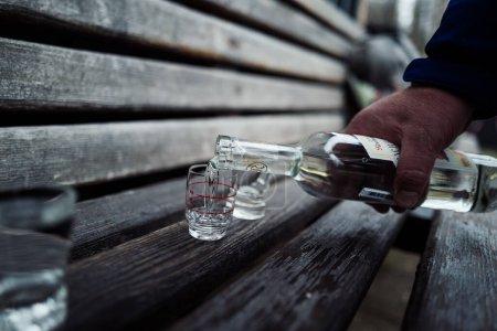 Photo for Pouring vodka in a glass on wooden bench - Royalty Free Image