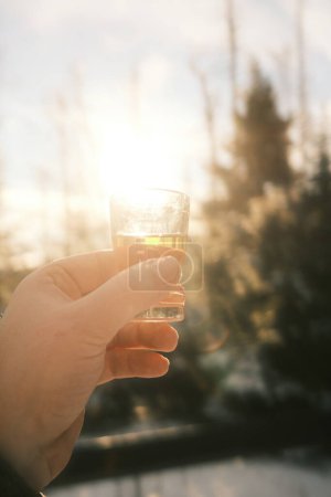 Téléchargez les photos : Un homme tient un verre de boisson dans sa main sur fond flou de paysage hivernal - en image libre de droit