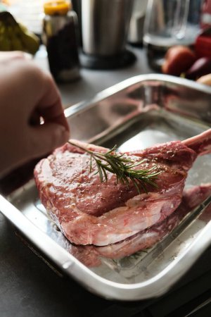 Téléchargez les photos : Gros plan de la main de l'homme mettant du romarin sur la viande d'agneau avec des épices - en image libre de droit