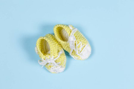 Photo for Yellow knitted baby shoes on a blue  background - Royalty Free Image
