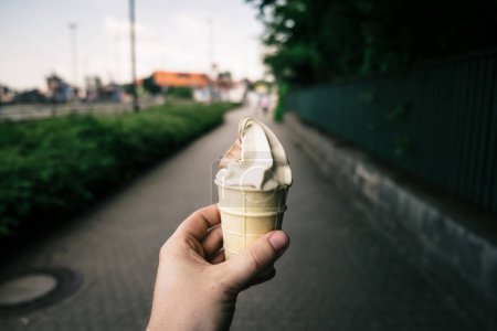 Foto de Una persona que sostiene un cono blanco de helado con fondo borroso. - Imagen libre de derechos