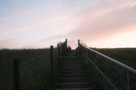 vista de ángulo bajo de la mujer de pie en la colina contra el cielo puesta del sol y los pasos en el campo 