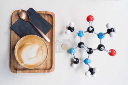 Caffeine (or theine) molecule made by molecular model next to milk coffee cup with latte art. Coffee and tea chemical formula with colored atoms and bonds