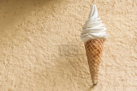 Téléchargez les photos : Figurine géante de cornet de crème glacée sur mur rugueux beige. Crème glacée publicité commerciale. - en image libre de droit