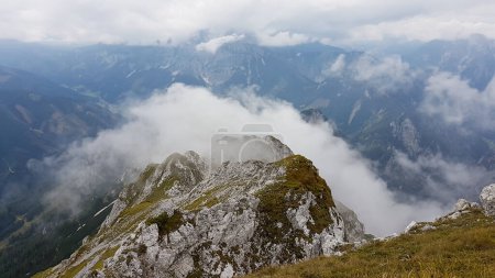 Photo for A panoramic view on the Austrian Alps from the Hochkogel peak. The valley below is shrouded with fog. Endless mountain chains. The slopes are overgrown with small plants. Mysterious landscape. - Royalty Free Image
