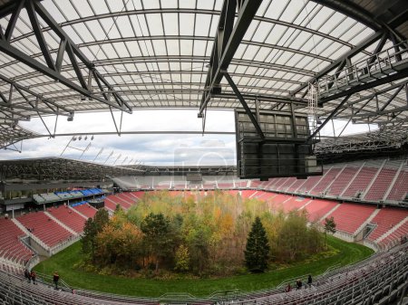 Téléchargez les photos : Une forêt plantée au milieu du stade de football à Klagenfurt, en Autriche. Le gazon de terrain ressemble à la forêt, changer de couleurs pour l'automne. Beaucoup de différentes sortes d'arbres. Installation moderne. Nature - en image libre de droit