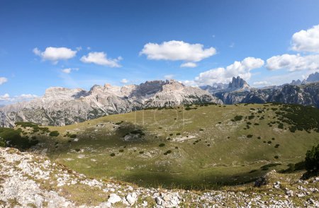 Foto de Una vista panorámica de un vasto valle en los Dolomitas italianos. Hay cadenas montañosas alrededor. El fondo del valle es verde exuberante. Unos pocos árboles en las laderas. Pocas nubes suaves en el cielo. Libertad - Imagen libre de derechos