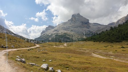 Téléchargez les photos : Une route gravelée qui traverse les Dolomites italiennes. Des montagnes hautes et pointues. Les pentes et les prairies sont dorées, les parties supérieures sont stériles et pierreuses. Couvert. Endroit isolé et désolé. Liberté - en image libre de droit
