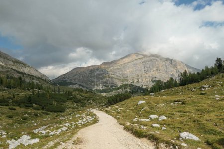Téléchargez les photos : Une route gravelée qui traverse les Dolomites italiennes. Des montagnes hautes et pointues. Les pentes et les prairies sont vertes, les parties supérieures sont stériles et pierreuses. Couvert. Endroit isolé et désolé. Liberté - en image libre de droit