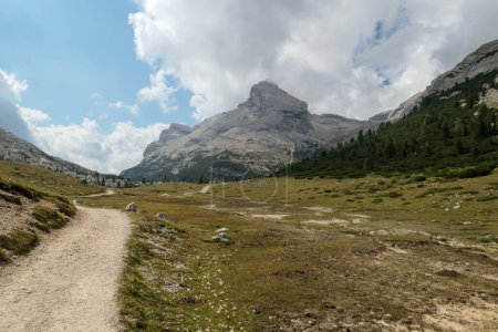 Téléchargez les photos : Une route gravelée qui traverse les Dolomites italiennes. Des montagnes hautes et pointues. Les pentes et les prairies sont vertes, les parties supérieures sont stériles et pierreuses. Couvert. Endroit isolé et désolé. Liberté - en image libre de droit