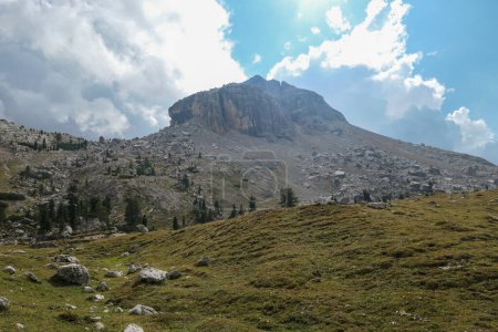 Téléchargez les photos : Vue rapprochée sur une montagne pierreuse et escarpée dans les Dolomites italiennes. La montagne massive est entourée de nuages. Quelques arbres envahissant ses parties inférieures. Zone éloignée et désolée. Couvert - en image libre de droit
