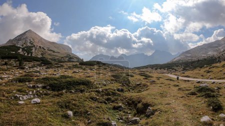 Téléchargez les photos : Une voie gravelée menant à travers les Dolomites italiennes. Des montagnes hautes et pointues. Les pentes et les prairies sont dorées, les parties supérieures sont stériles et pierreuses. Endroit isolé et désolé. Liberté et calme - en image libre de droit