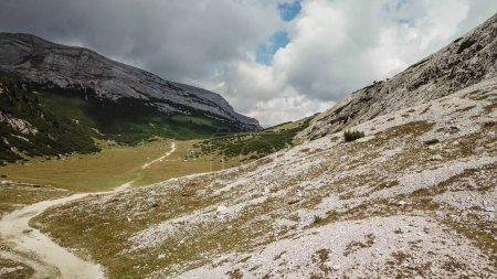 Téléchargez les photos : Une voie gravelée menant à travers les Dolomites italiennes. Des montagnes hautes et pointues. Les pentes et les prairies sont dorées, les parties supérieures sont stériles et pierreuses. Endroit isolé et désolé. Liberté et calme - en image libre de droit