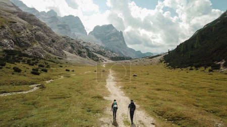 Foto de Un par de senderismo a lo largo de un camino que conduce a través de un valle en Dolomitas italianas. Montañas altas y afiladas alrededor. Paisaje pedregoso y crudo, prado verde. Lugar remoto y desolado. Libertad de exploración - Imagen libre de derechos