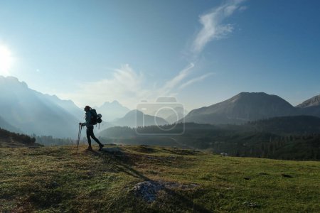 Photo for A woman enjoying an early morning in Italian Dolomites. The valley below is shrouded in morning haze. In the back there are high mountain chains. Sun slowly rising above the peaks. Golden hour - Royalty Free Image