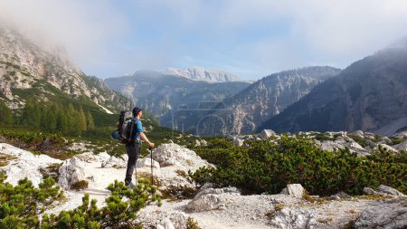 Téléchargez les photos : Un homme avec un grand sac à dos de randonnée profitant de la vue panoramique sur les Dolomites italiennes. Il se dresse sur un plateau pierreux, au-dessus de la vallée. Quelques nuages autour. Dans les chaînes de haute montagne arrière. Liberté - en image libre de droit