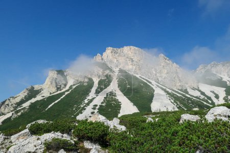 Téléchargez les photos : Vue lointaine sur une haute montagne dans les Dolomites italiennes. Le sommet de la montagne est entouré de quelques nuages. Il a des pentes très raides, plein de glissements de terrain et de perdre des pierres. Haute alpinisme. Expérience - en image libre de droit