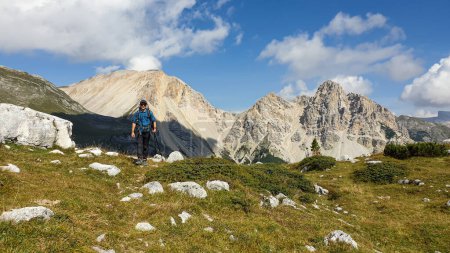 Téléchargez les photos : Un homme avec un grand sac à dos de randonnée profitant de la vue panoramique sur les Dolomites italiennes. Il se promène sur un plateau pierreux, au-dessus de la vallée. Quelques nuages autour. Dans les chaînes de haute montagne arrière. Liberté - en image libre de droit