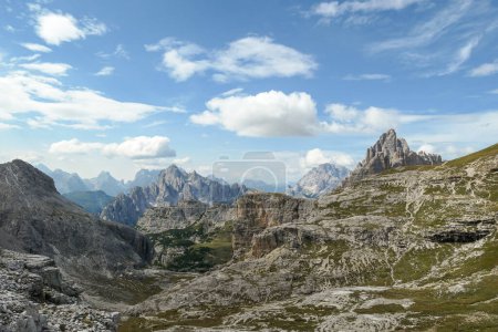 Photo for An endless view on a high and desolated mountain peaks in Italian Dolomites. The lower parts of the mountains are overgrown with moss and grass. Raw and unspoiled landscape. Few clouds above the peaks - Royalty Free Image