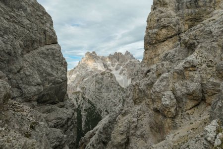 Photo for A sneak-peak on a high and distant mountain in Italian Dolomites. The mountain is visible between two rocky and steep slopes in front. Playing hide and seek. Raw and desolate landscape. Overcast - Royalty Free Image