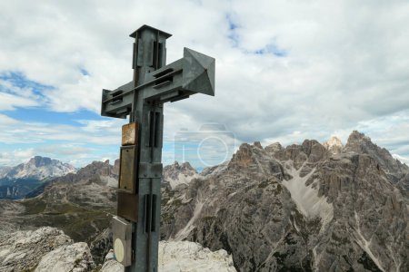 Photo for A wooden cross on high and desolated mountain peak in Italian Dolomites. In the back there are endless mountain chains. Raw and unspoiled landscape. Few clouds above the peaks. Sharp and steep slopes. - Royalty Free Image