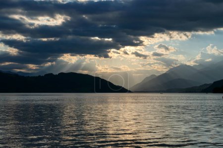 Photo for A sunset by Millstaetter lake in Austria. The lake is surrounded by high Alps. Calm surface of the lake reflecting the sunbeams. The sun sets behind the mountains. Thick clouds above. Natural beauty - Royalty Free Image