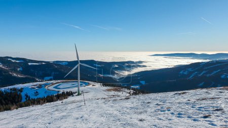 Foto de An early, wintery morning in the region of Stubalpe, Austria. The whole area is covered with powder snow. There is an artificial lake, covered with thin layer of ice and a windmill next to it. Sunny - Imagen libre de derechos