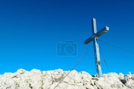 Photo for A metal cross of the top of Mittagskogel in Austrian Alps. Clear and sunny day. Endless mountain chains. Outdoor activity. Barren top of the mountains, lush lower parts. Achievement and completion - Royalty Free Image