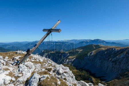 Téléchargez les photos : A wooden cross on top of Hohe Weichsel, Alpine peak in Austria. The cross is leaning, as if it was going to fall. There are endless mountain chains behind it. Early fall. The slopes are turning golden - en image libre de droit