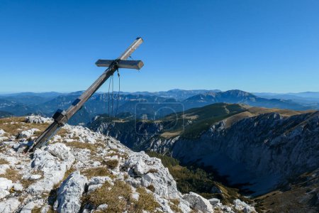 Téléchargez les photos : A wooden cross on top of Hohe Weichsel, Alpine peak in Austria. The cross is leaning, as if it was going to fall. There are endless mountain chains behind it. Early fall. The slopes are turning golden - en image libre de droit