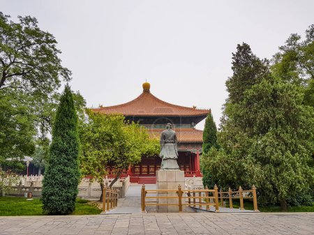 Téléchargez les photos : Confucius temple in Beijing, China, painted red. There is Confucius statute in front of the temple. The stature of the philosopher is surrounded by golden railing. Lots of trees around. Tradition - en image libre de droit