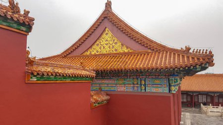 Photo for A close up on a red wall inside of Forbidden City in Beijing, China. The building has very richly decorated rooftop, with elements of gold. Peace and calmness. Overcast due to the air pollution. - Royalty Free Image
