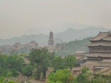 Photo for A panoramic view on a small village in northern China. A tall pagoda striking above the village.  There is a dense forest around. Rural areas. Tradition meets modernisation. Overcast and air pollution - Royalty Free Image