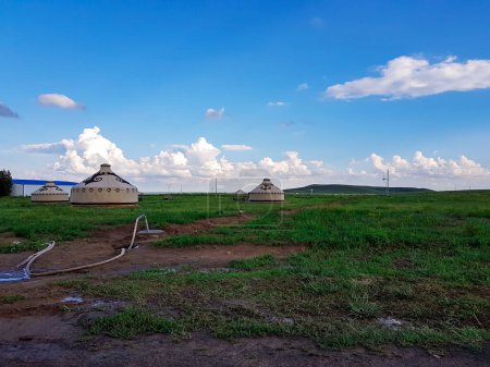 Foto de A few white, traditional yurts located on a pasture in Xilinhot in Inner Mongolia. Endless grassland. Blue sky with a few thick, white clouds. A long garden hose in front. Nomadic way of life. - Imagen libre de derechos