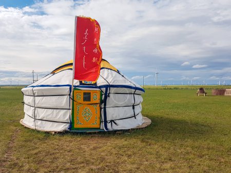 Foto de A white, traditional yurt located on a pasture in Xilinhot in Inner Mongolia, with a big red flag attached to it. Endless grassland. Wind turbines in the back. Clean energy. Nomadic way of life - Imagen libre de derechos