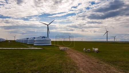 Foto de A few white, traditional yurts located on a pasture in Xilinhot in Inner Mongolia. Endless grassland. Blue sky with a few thick clouds. Wind turbines in the back. Clean energy. Nomadic way of life. - Imagen libre de derechos