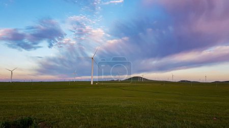 Photo for A panoramic view on a hilly landscape of Xilinhot in Inner Mongolia. Endless grassland with a few wind turbines in the back. The sun starts to set, coloring the sky pink. Thick, rainy clouds. - Royalty Free Image