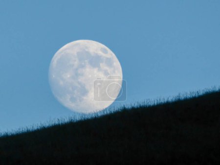 Photo for A full moon rising above the hilly grassland in the nearby of Xilinhot, Inner Mongolia, China. The sky behind it is cloudless and light blue. Rounded face of the moon. New moon. Calmness - Royalty Free Image