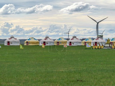 Foto de Yellow and white traditional yurts located on a pasture in Xilinhot in Inner Mongolia. Endless grassland. Blue sky with a few thick clouds. Wind turbines in the back. Clean energy. Nomadic way of life - Imagen libre de derechos