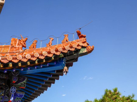 Foto de A close up on the rooftop of a pavilion in Summer Palace in Beijing, China. The roof has orange tiles and decorative small figures of guardians at the edges. A few tree branches on the side. Blue sky - Imagen libre de derechos
