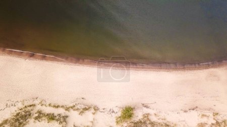 Foto de A top down drone shot of the sandy beach by the Baltic Sea on Sobieszewo island, Poland. The waves are gently rushing to the shore. The beach is overgrown with some bushes and grass. Waves meditation - Imagen libre de derechos