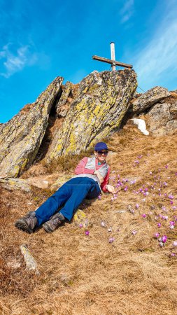 Foto de Una mujer acostada en el pasto dorado, rodeada de azafranes púrpura en la región de Sauofen en los Alpes austríacos. Primavera en prados alpinos. Hay un muro de piedra detrás de ella. La naturaleza despierta - Imagen libre de derechos