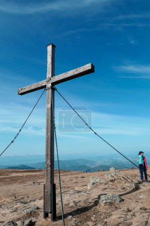 Foto de A woman with hiking backpack standing under a wooden cross on top of Sauofen in Austrian Alps. A vast, golden pasture around. Fall vibes. She is laughing, being happy. Reaching the top. Serenity - Imagen libre de derechos