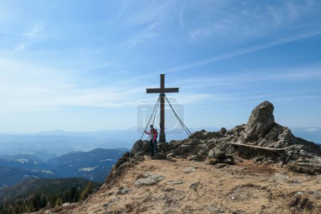 Foto de Una mujer con una mochila de senderismo que llega a la cima de Sauofen en los Alpes austríacos. Una cruz de madera encima. Montones de piedras alrededor. Vibras de otoño. Cadenas de alta montaña en la parte posterior. Serenidad y logro - Imagen libre de derechos