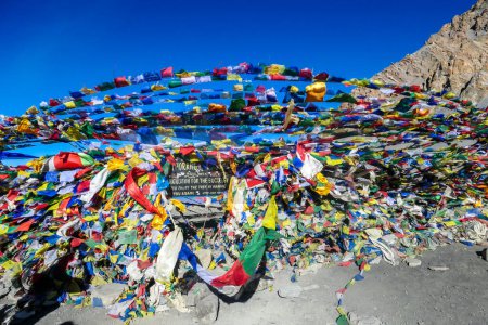 Foto de The waving flags at the top of Thorung La Pass, Annapurna Circuit Trek Nepal. Congratulations for the effort. Colorful prayer flags attached to the stone wall, blow by the wind. Clear sky. Achievement - Imagen libre de derechos