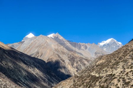 Téléchargez les photos : Vue sur la haute Himalaya le long du circuit de l'Annapurna Trek, Népal. Paysage aride et aride autour. Ciel clair et bleu. La haute Himalaya s'étend autour. Des montagnes enneigées. Sérénité et calme - en image libre de droit
