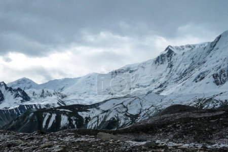 Téléchargez les photos : Stormy weather in snow capped Himalayan peaks along Annapurna Circuit in Nepal. Barren and sharp slopes. Mountains are partially shrouded with clouds. Exploration and discovering new places. Coldness - en image libre de droit